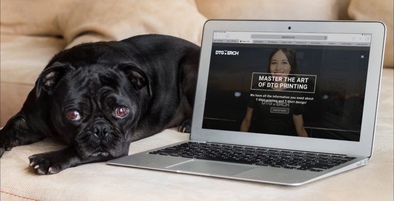Black dog next to a lap top computer. On screen, the DTG Merch blog page.